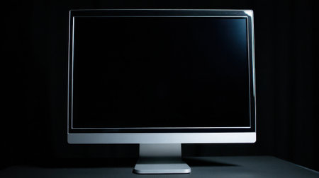 A stylish computer monitor stands still in a dark room emphasizing its sleek design and modern appeal.の素材
