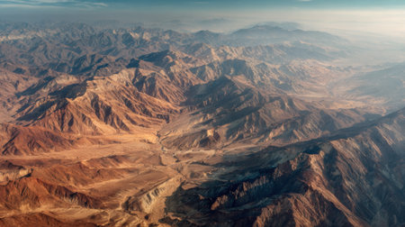A stunning aerial scene captures vast mountain ranges with jagged peaks and deep valleys. The soft morning light reveals intricate patterns in the terrain showing natures beauty.の素材