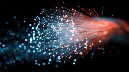Vibrant strands of fiber optics emit blue and orange light creating a stunning glow against a dark background. This captivating scene illustrates technologies beauty.の素材