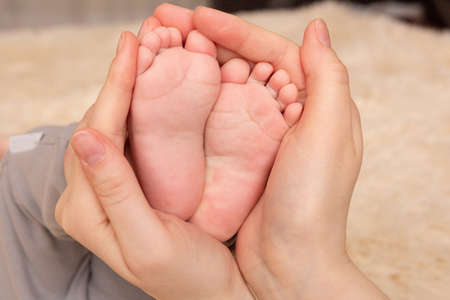 Baby feet in mother hands. Tiny Newborn Baby's feet on female Shaped hands closeup. Mom and her Child. Happy family concept. Beautiful conceptual image of maternityの写真素材