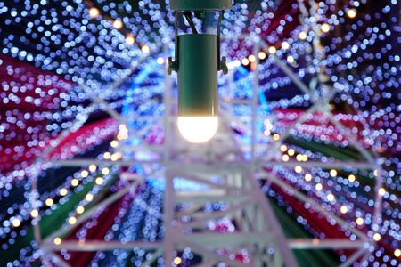 A single light bulb in socket with bokeh festive lights background.の写真素材