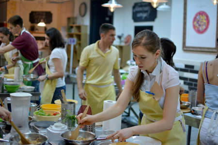 KYIV, UKRAINE - December 13, 2014: Happy group of friends with male chef cook cooking and talking in kitchen. Cooking class.のeditorial素材