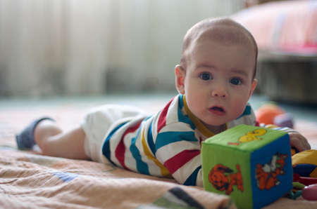 Cute little baby with big brown beautiful eyes laying on floor with kids colorful toys.Candid image of young baby playing at homeの写真素材