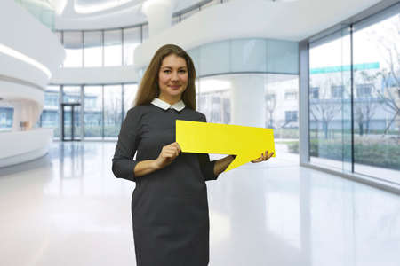 The Smiling young woman in business dress holding a yellow plate in hand on a light office background. Businesswoman showing blank yellow banner for inscriptions. Close-up,clear business conceptの写真素材