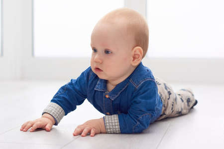 Portrait of a cute little baby in blue denim shirt laying on the floor. Candid image of young baby playing at homeの写真素材