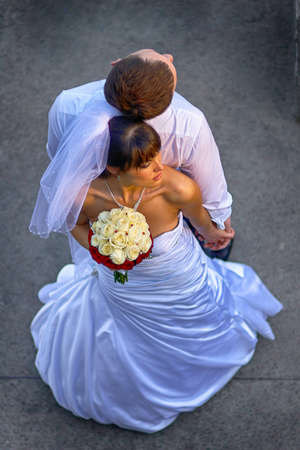 Newly wedded couple leaning back to back and hold hands. Outdoor shot of a Bride with a bouquet of yellow white red flowers.の写真素材