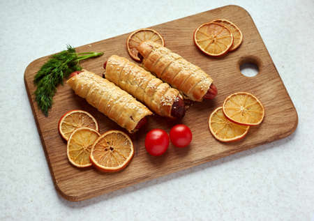 Baked sausages wrapped in puff pastry on a wooden cutting board accompanied by parsley,tomatoes and dried orange slices.Pigs in blanket,sausage rollsの写真素材