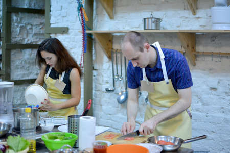 Two happy man and woman cooking and talking in the kitchen. Culinary, food and people, cooking class conceptの写真素材