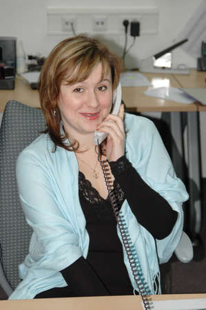 Beautiful business woman talking on phone at her desk in an officeの写真素材