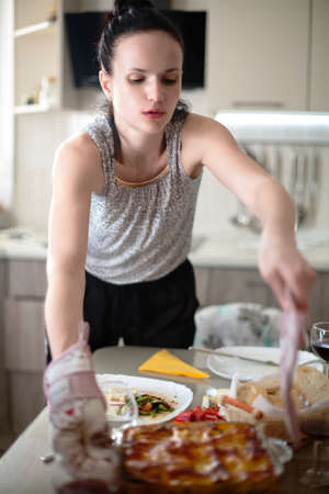 Beautiful Caucasian smiling woman putting a plate with meal on dining table at home/Woman serving food while preparing dining table for family lunch in the kitchenの写真素材