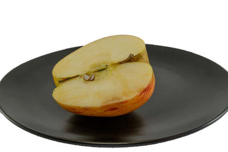 Half of an apple on a black plate with white backgroundの写真素材