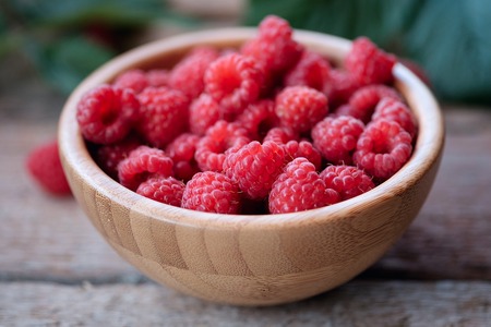 Organic raspberries in bowl on wood background.
