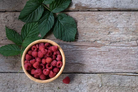 Organic raspberries in bowl with leaf. Wood background. Top viewの写真素材