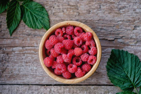 Organic raspberries in bowl with leaf. Wood background. Top viewの写真素材