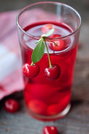 Glass of cherry juice or compote on wooden table with cherriesの写真素材