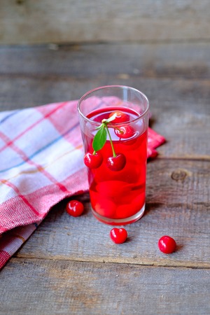 Glass of cherry juice or compote on wooden table with cherriesの写真素材
