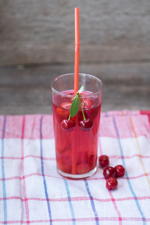 Glass of cherry juice or compote on wooden table with cherriesの写真素材