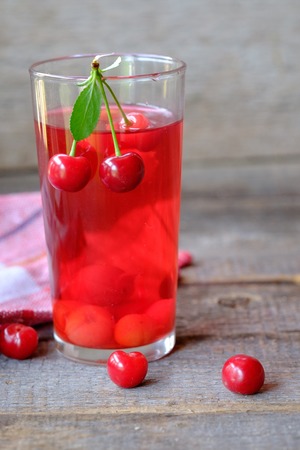 Glass of cherry juice or compote on wooden table with cherriesの写真素材
