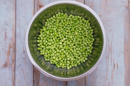 Green peas in metal bowl on wooden background, top view. Rustic table backgroundの写真素材