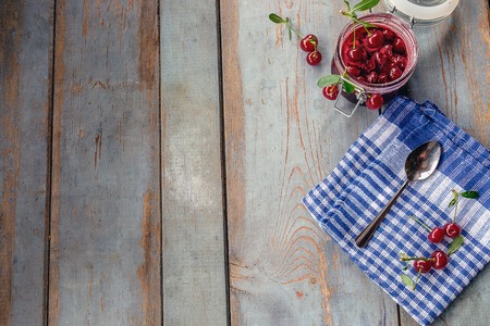 Jar of cherry jam and some cherries on the blue napkin. Rustic table backgroundの写真素材
