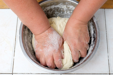 Woman's hands knead dough on a metal bowlの写真素材