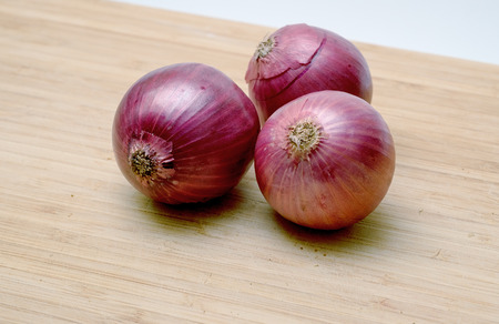 Three red onions isolated on wooden backgroundの写真素材