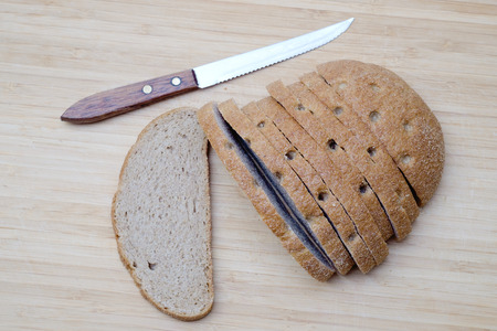 Sliced fresh brown bread and knife on wooden desk. Top viewの写真素材