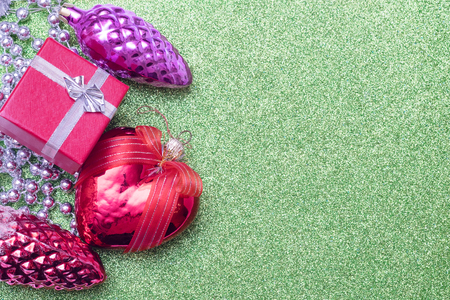 Three christmas toy bump, christmas heart shaped red ball and small red gift box on green background. Empty space for textの写真素材