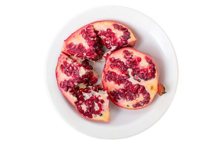 Broken red ripe juicy pomegranates in white plate on white bakcground. Vegetarian fruit healthy background concept.の写真素材