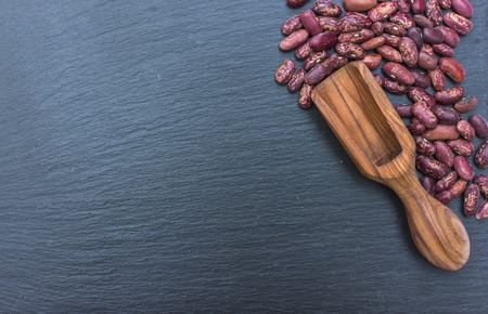 Organic red beans and olive wood scoop on black background of slate or stone. free Space for your text.の写真素材