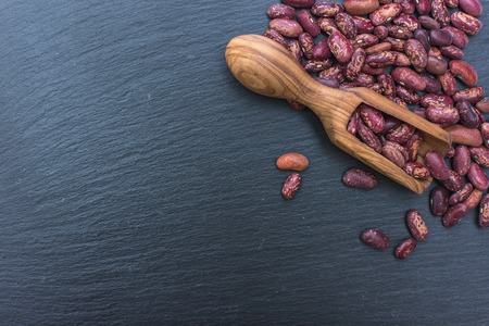 Organic red beans and olive wood scoop on black background of slate or stone. free Space for your...