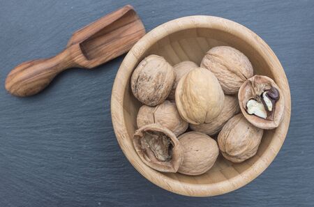 Walnuts and olive wood scoop in a wooden bowl on black background of slate or stone