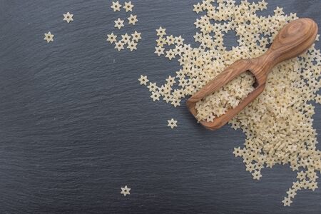 Star shaped noodles and olive wood scoop on black background of slate or stone. Top viewの写真素材