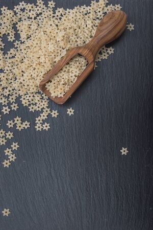 Star shaped noodles and olive wood scoop on black background of slate or stone. Top viewの写真素材