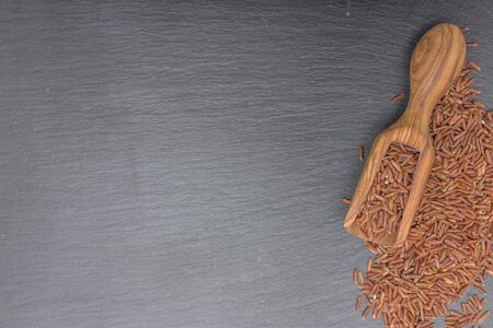 Red rice and olive wood scoop on black background of slate or stone. Top viewの写真素材