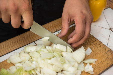 Male hand cutting onion on a wooden cutting board. Close up image