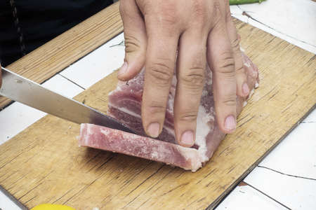Cutting a piece of meat on a wooden cutting board. Close up image