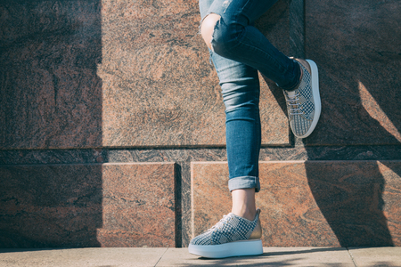 The girl is standing by the wall in fashionable sneakersの写真素材