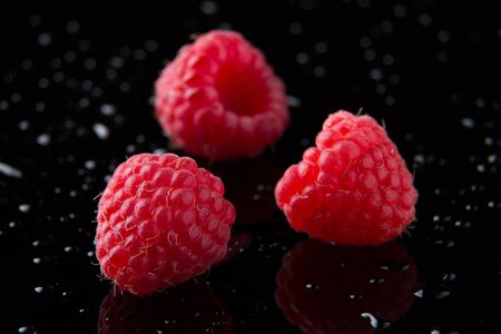 Ripe berry raspberries on a black background. Three raspberry berries