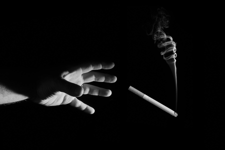 A man's hand reaches for a cigarette on a black backgroundの写真素材