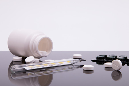 Medicines and a thermometer on the mirror surface of the table.の写真素材