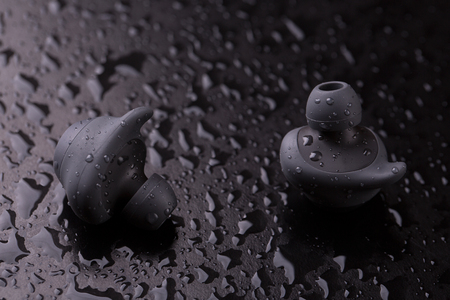 Intra-channel Bluetooth headphones on a dark background with water drops.の写真素材