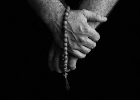 Church rosaries in the hands of men on a black background.の写真素材