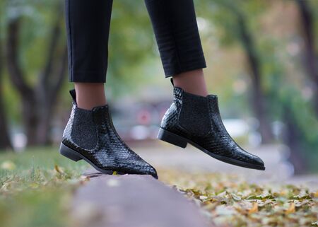 Python boots on the girl’s legs. Girl walking in the park in reptile leather shoes.