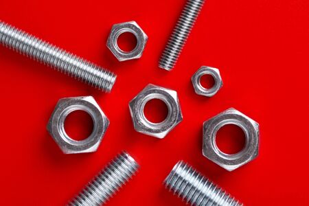 Bolts and nuts on a red background. Nuts and bolts top view.