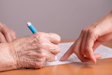Elderly woman signs a paper document. Signing papers. An elderly man signs a document.の写真素材