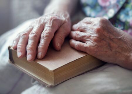 An elderly woman holds an old book in her hands.の写真素材
