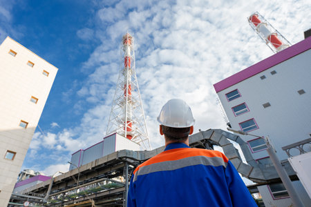 An engineer in work clothes and a construction helmet looks at large chimneys.
