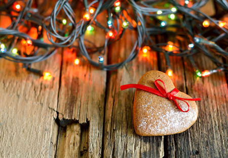 Gingerbread Xmas heart on an old weathered wooden background in a garland lightsの写真素材