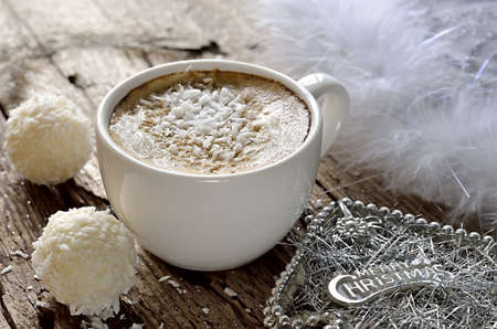 White coffee cup with coconut dessert on weathered wooden glittering surface with Christmas decorationsの写真素材